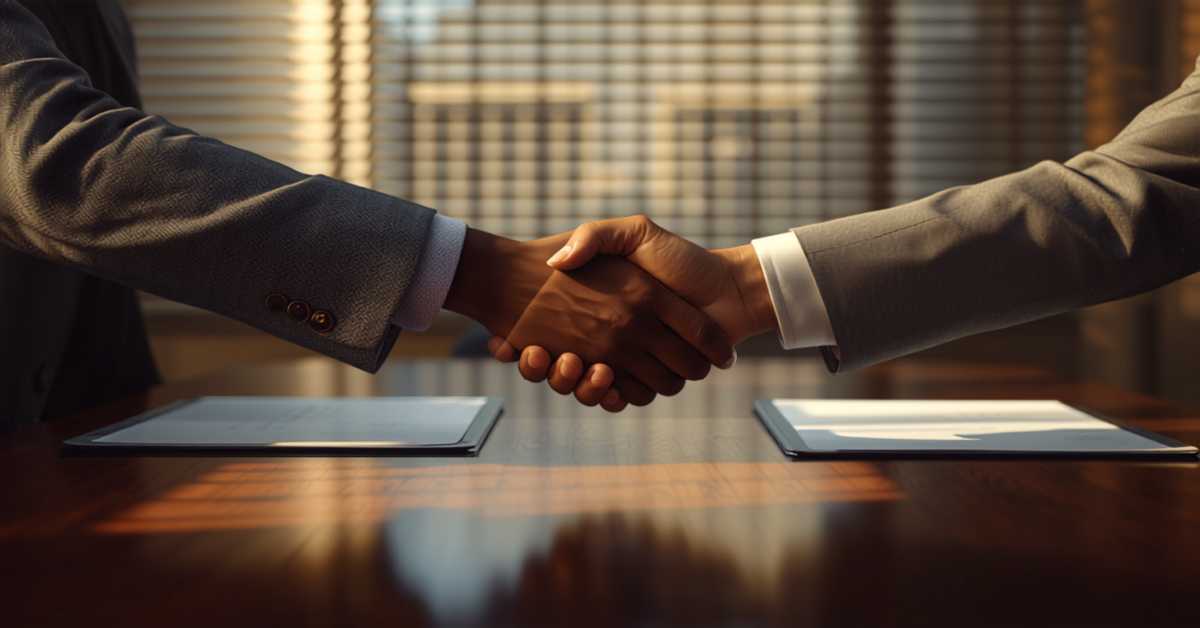 Two professionals shaking hands over a desk with legal documents